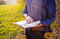 Man Wearing Blue and Black Flannel Shirt Holding White and Black Book during Daytime