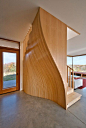 Inside this house, a staircase is screened behind an undulating timber wall