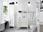 白色浴室内装饰着瓷砖，并配有一个洗脸池柜和一个镜面柜门高柜。与它们搭配的有一个白色洗脸池和一个镜面柜门壁柜。
