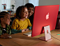 大人和孩子在房间内欢笑着与木质台面上的 iMac 进行交互，机身背面为深粉色外观。