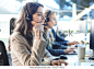 Female customer support operator with headset and smiling, with collegues at background