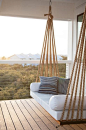 Chic covered second floor balcony is fitted with a rope swing bed adorned with plush white cushions and blue striped pillows.