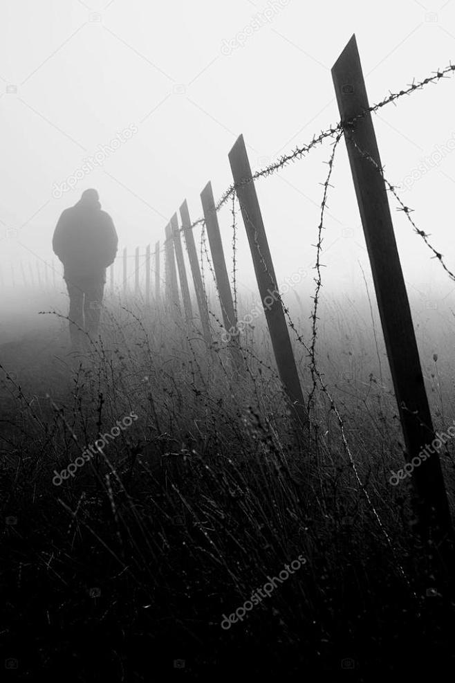 在浓雾中带刺铁丝网围栏附近有个男人