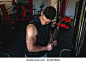 One man side view caucasian male bodybuilder at gym wearing black shirt workout using rope and cable weights for arms exercise triceps training copy space waist up dark photo real people amateur