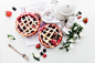 An overhead shot of strawberry and blackberry pies next to a white coffee pot and a bunch of flowers