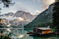 A log cabin lakehouse and dock on Lago di Braies with the snow-capped mountains in the background