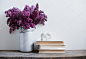 家居室内装饰，丁香在花瓶和质朴的木桌，白色的墙壁背景上的书