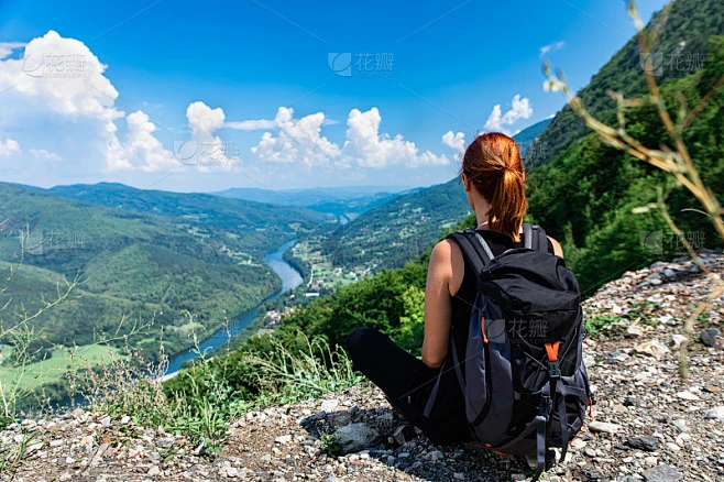 女徒步旅行者背着背包坐在山顶欣赏风景。素材-花瓣网