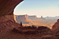This may contain: a person standing at the end of a cave looking out over desert land and mountains