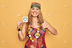 漂亮的金发嬉皮女人戴着太阳镜和配件拿着提醒与心的快乐和积极的微笑，大拇指做优秀和赞同的标志