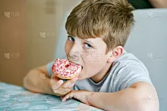 快乐的青春期男孩在室内吃甜甜圈。金发小孩在家庭厨房或学校食堂可爱的孩子和不健康的含糖食品。