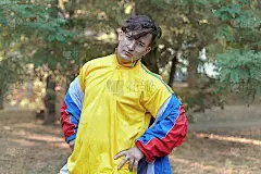 年轻英俊的白人男子与明亮的怪胎运动装70年代风格站在一个早晨的公园。