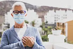 一位戴着外科口罩的老妇人把手放在他的心脏上向他问好。世界卫生组织针对新冠肺炎大流行推荐的新的问候方式