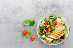 烤鸡胸肉，鱼片和新鲜蔬菜沙拉生菜，芝麻菜，菠菜，黄瓜和番茄。健康的午餐菜单。减肥食品。俯视图