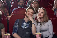 严肃的女人和微笑的男人在现代电影院看电影。