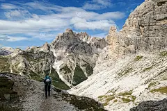 一名女子背着背包，拄着拐杖在意大利Dolomites的一条小路上徒步旅行。周围有陡峭的山脉。山坡低处