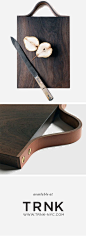 A handcrafted walnut serving board with a saddle leather handle.: 