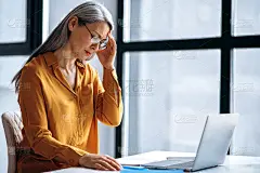 伤心的亚洲中年女商人或女家教，厌倦了在线加班，或进行远程教学，闭上眼睛，头痛，需要休息