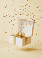 Empty open gift box mockup, white and gold color palette, gold ribbon around the top of it with some falling confetti on the floor, background is light yellow and beige, soft studio lighting, high-resolution photography, hyper-realistic, ultra-detailed.