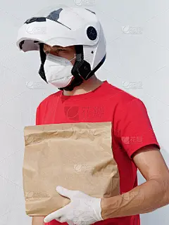 穿着制服的摩托车送货员。装有医用防护手套和kn95口罩的纸板袋。网上购物和快递。