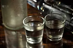 瓶子旁边放着冰冻的酒精杯。在深棕色的桌子上喝酒。黑色背景上的透明器皿。玻璃下的破旧木板。