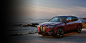 A 2024 BMW iX all-electric sports utility vehicle in Aventurin Red Metallic parked beside a beach overlooking the sea