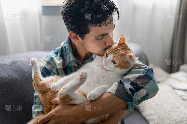 年轻人把一只棕白相间的猫抱在怀里并亲吻它。