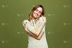 快乐轻松的年轻女子拥抱自己微笑在绿色的背景。自爱，自我照顾，身体积极向上