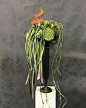 This may contain: a tall black vase filled with lots of green and red flowers on top of a white block