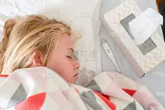 一个生病的十几岁的女孩躺在床上，毯子上盖着温度计