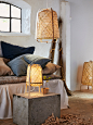 A sofa with cushions in a rustic-looking room that has matching, lit lamps in woven bamboo, including KNIXHULT table lamp.