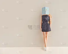 身穿灰色连衣裙的金发美女玩偶站在淡黄色的墙壁前，头上系着一本书。最小的创造性阅读概念与复制空间。爱书