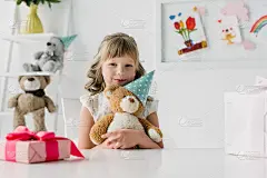 可爱的生日孩子抱着锥形泰迪熊在桌子上与礼盒