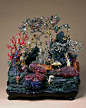 孔雀石嵌珠宝蓬莱仙境盆景 
清乾隆，造办处造，通高43cm，座高5cm，座径41.5－30cm。清宫旧藏。紫檀木座上，苍绿的孔雀石垒山垫底，孔雀石前以大小红、蓝宝石堆砌成湖石。孔雀石山前景平台上遍植金银宝石制作的灵花仙草，仅灵芝即有异形珍珠、金累丝嵌宝石和珊瑚雕刻3种。山前后还有银烧蓝梅树、银镀金松树、珊瑚树和银镀金桃树，树上缀有珍珠花和碧玺桃果等。山间树下立白玉雕寿星、侍童及鹿，左侧梅树下立抱如意的铜镀金侍童，右侧松树下立背驮珍珠宝石的铜镀金仙鹤，这些金玉珠宝的造型共同构成洞天福地的景观。《史纪·秦始皇