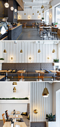 In this modern coffee shop, gold has been carried through the space with simple gold pendant lights that hang above the tables. A corrugated white wall and upholstered grey banquettes add texture to the space, while the wood tables and chairs tie in with 