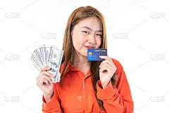 美丽的亚洲年轻女子高兴地微笑，在她的一只手拿着大量的美元，她从她的信用卡在她的另一只手-信用卡支付网