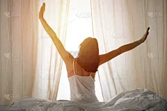女人在床上伸开双手醒来后，太阳耀斑。深色头发的女人进入一个愉快和放松的一天后，睡了一个好觉和后视图。