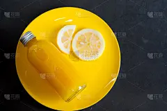瓶中的新鲜橙汁和熟透多汁的柠檬切片放在黄色的盘子里。创意夏日饮品简约背景