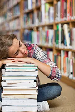一个学生坐在图书馆的地板上，靠在一堆书上打瞌睡