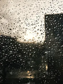 阳光下的雨滴落在窗玻璃上。雨滴和阳光在玻璃上的美丽形象与建筑物和城市街道的观点。手机照片。垂直的壁纸
