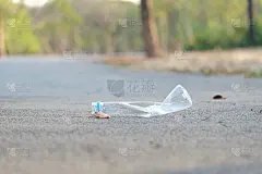 一个塑料瓶的饮用水乱丢在街道的底层，在绿色公园和绿色自然的背景