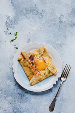 早餐可丽饼配煎蛋、奶酪、培根和大葱，背景是浅灰色的混凝土。