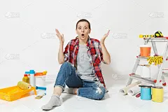 困惑、烦恼、疲倦、震惊的女人坐在地板上，用仪器装修公寓孤立在白色的背景上。墙纸，胶水配件，油漆工具。