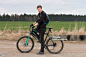 Young man on mountain bike on spring trip. Young man on mountain bike stands on path, on background green meadow and forest. Young man on mountain bike stands on path, on background green meadow and forest. Active Lifestyle Stock Photo