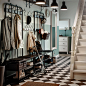 Traditional hallway with black and white chequered floor and two black coat racks and shoe storage benches side by side.