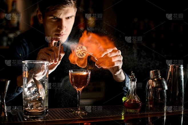 年轻的调酒师专业地在鸡尾酒中洒上燃烧的柑橘片。素材-花瓣网
