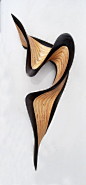 Wenge Jive by Kerry Vesper. This wood sculpture ripples across the wall with a flourish. The artist hand cuts layers of Baltic birch and *wenge wood*, then meticulously stacks and glues them together before carving and sanding them into the final form. Th