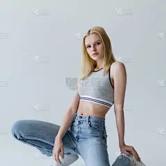 Trendy young woman in top and jeans posing on grey