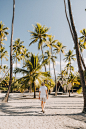 woman in white dress walking on gray concrete pathway between palm trees during daytime