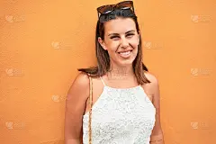 美丽的女孩倚在橘色的墙壁上，年轻友好的女人在一个阳光明媚的夏天快乐地微笑着